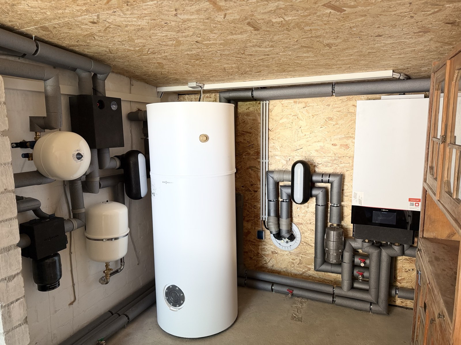 Technikraum mit Wärmepumpen-Inneneinheit, Speicher und Verrohrung